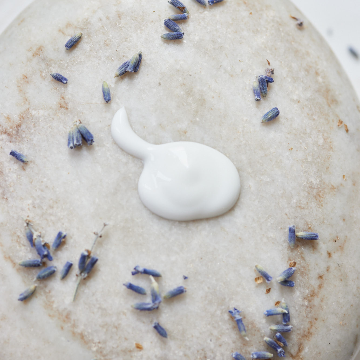 Texture de la crème à mains lavande sur une pierre greige et des brins de lavande